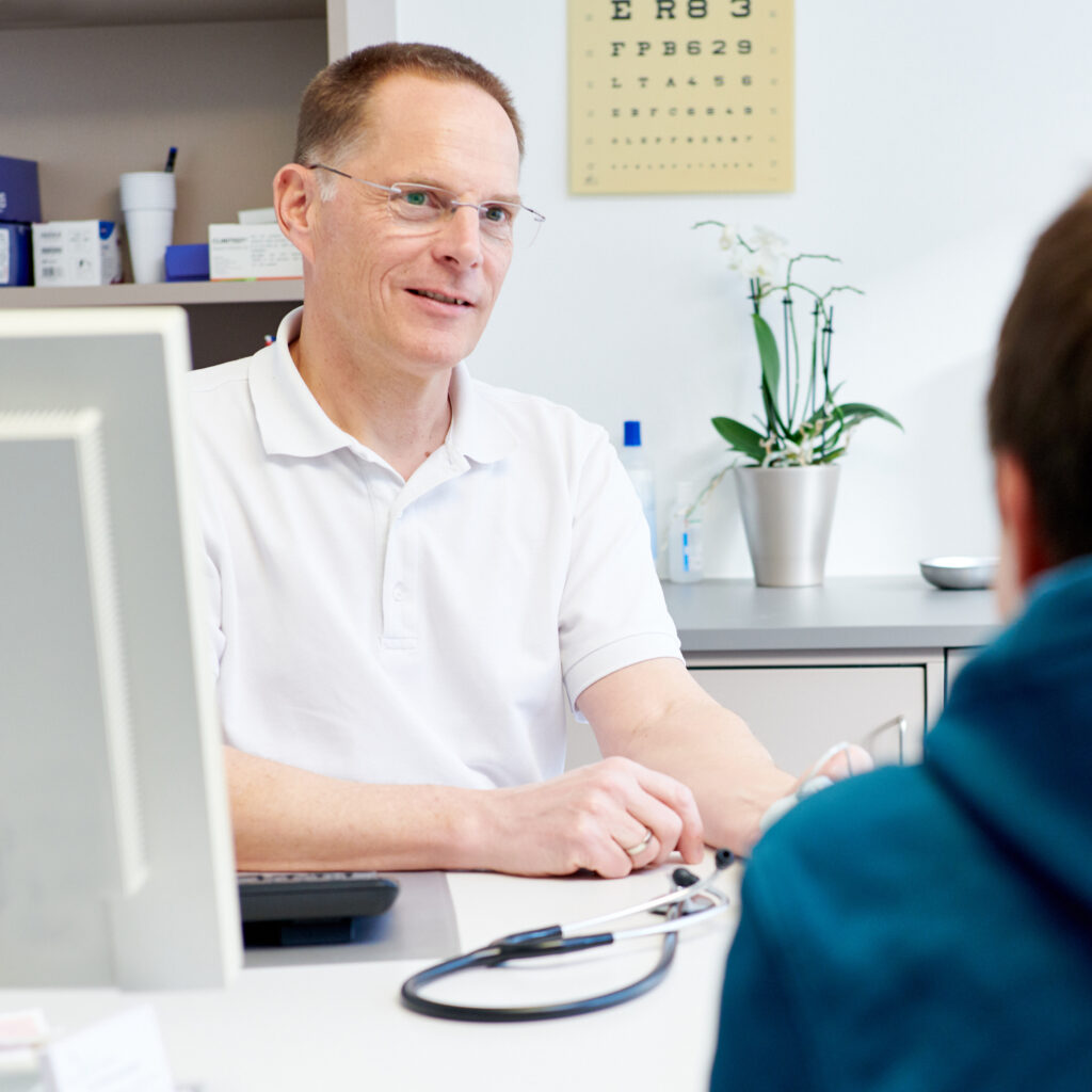 Arzt sitzt am Schreibtisch und berät einen Patienten